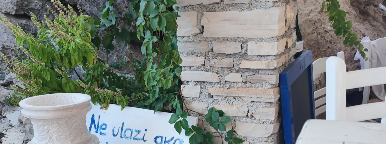 Charming Dubrovnik detail: White stone planter with handwritten sign in Croatian, green ivy, and rustic wall texture