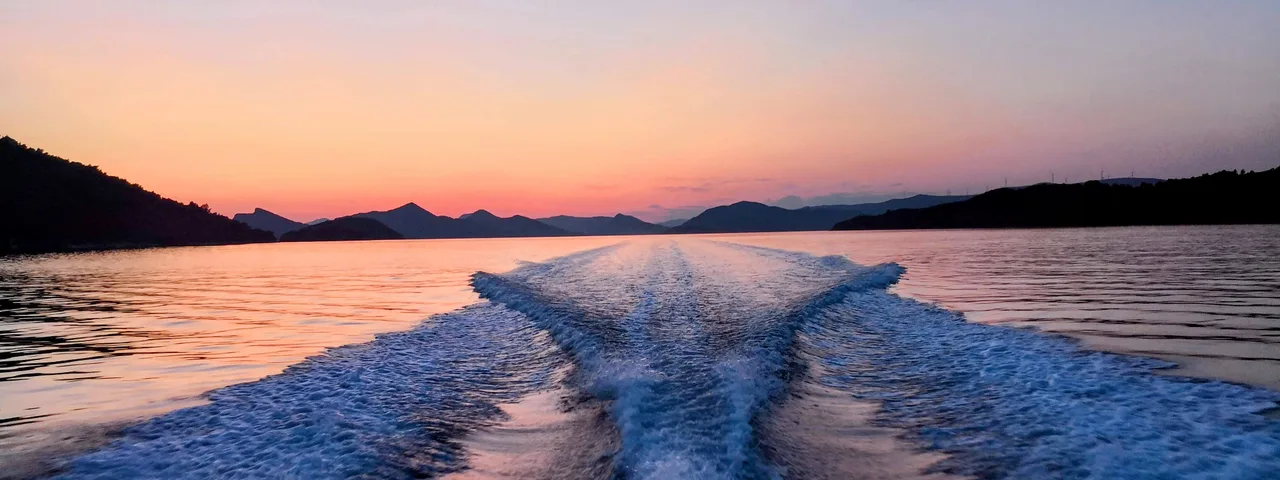 Sunset view from a boat, showing wake trails on calm water surrounded by silhouetted Elaphite islands.