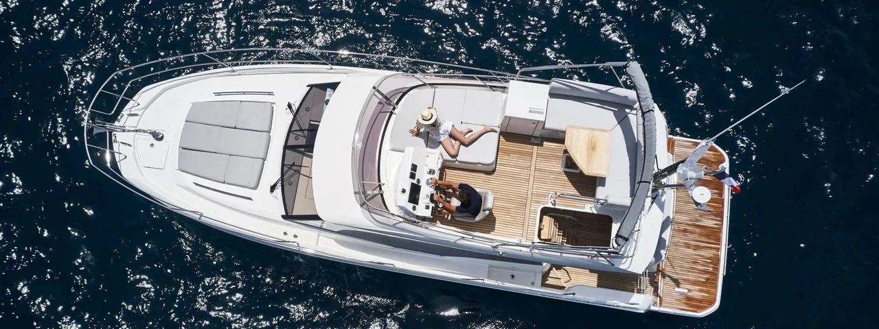 Aerial view of a luxury yacht from our fleet sailing in crystal-clear blue waters, featuring multiple decks, spacious lounging areas, and a sleek white exterior.