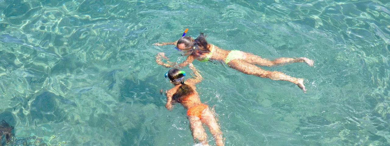 Two people snorkeling in crystal-clear turquoise waters near Blue Cave on a sunny day.