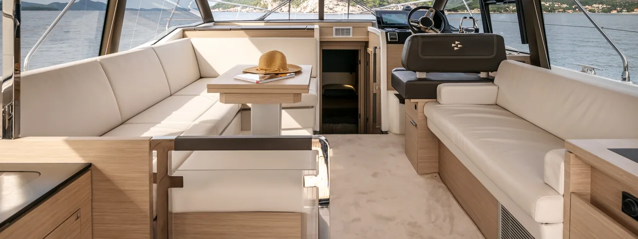 Spacious luxury yacht interior salon with dining table, comfortable lounge seating, and panoramic sea views of the Croatian coast.