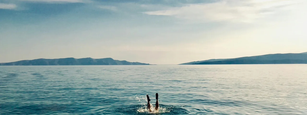 Person diving into the clear turquoise Adriatic Sea with distant islands, showcasing a refreshing private boat tour experience in Croatia.