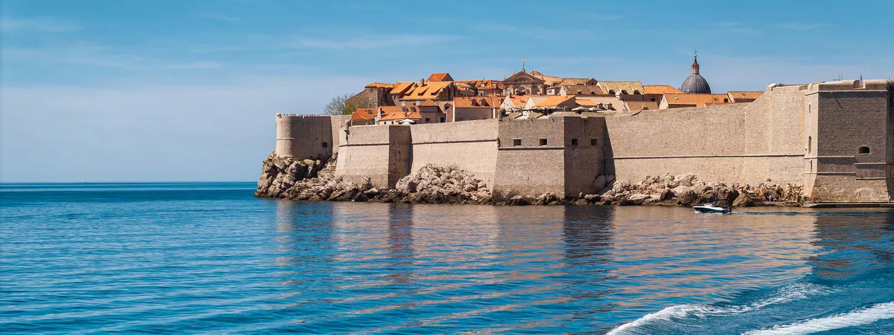 Luxury speedboat cruising on the blue Adriatic Sea with historic Dubrovnik city walls and Old Town in the background, Croatia.
