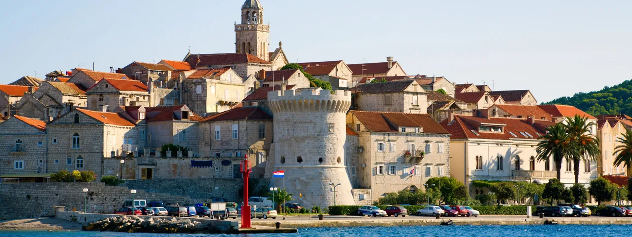 Korčula old town waterfront with medieval defensive walls and St Mark's Cathedral bell tower rising above the calm Adriatic Sea