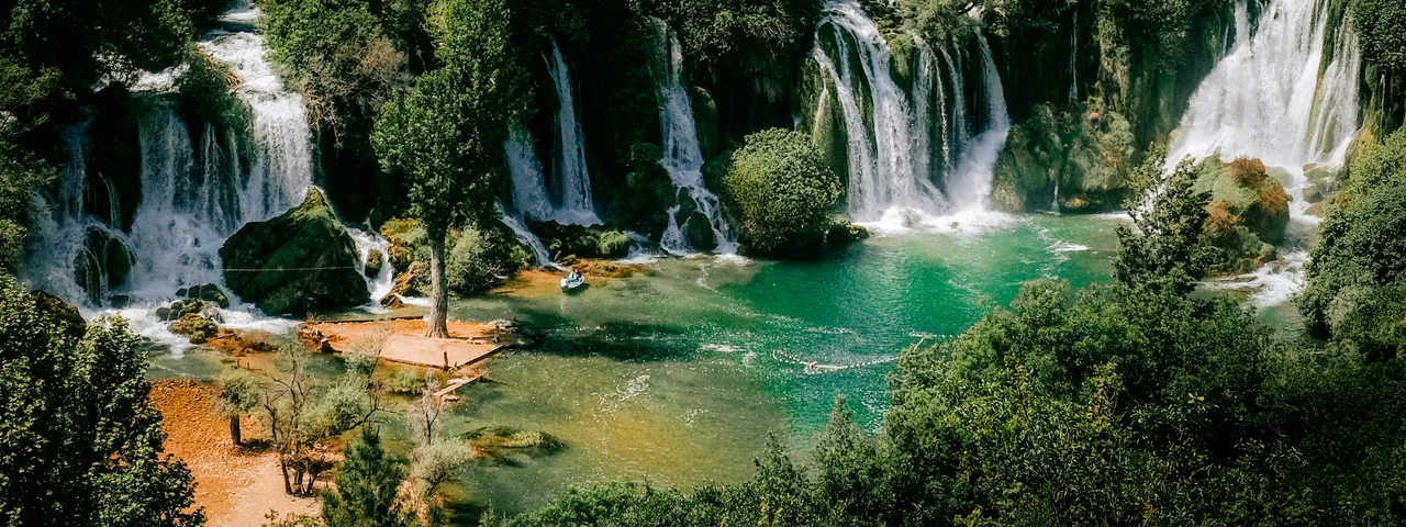 Turquoise swimming pool beneath Kravice Waterfalls on a sunny summer day in Bosnia and Herzegovina