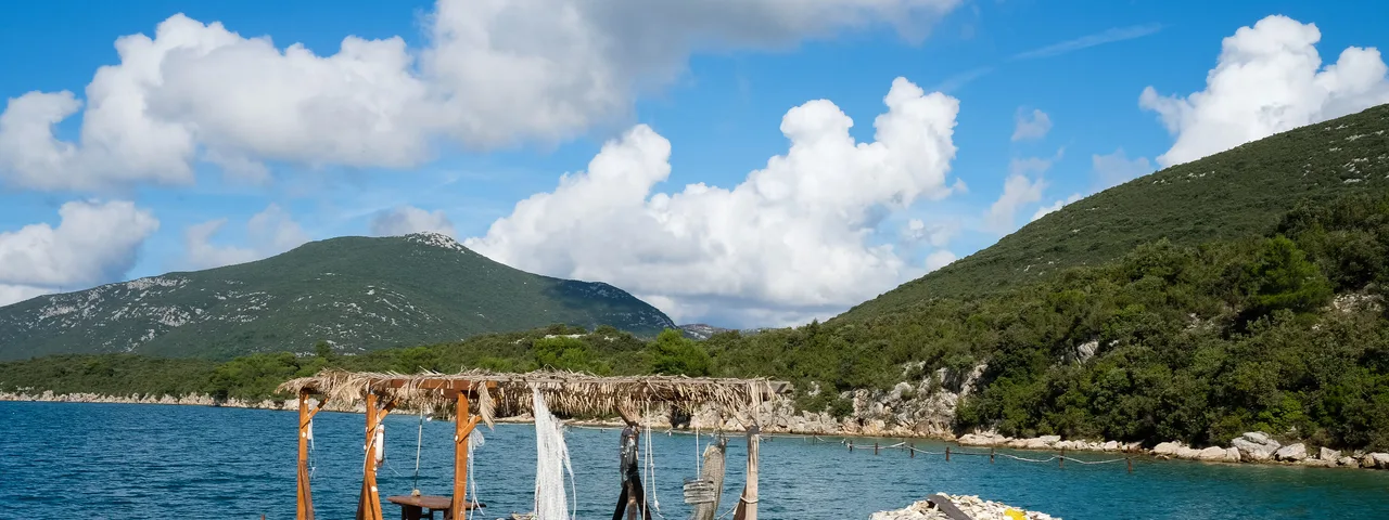 Oyster farming raft floating on calm turquoise Mali Ston Bay with a lone worker tending nets and oyster clusters, Croatia