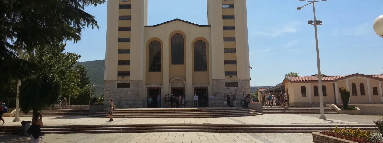 Crowd of pilgrims gathered around the Virgin Mary statue on Apparition Hill with panoramic village view