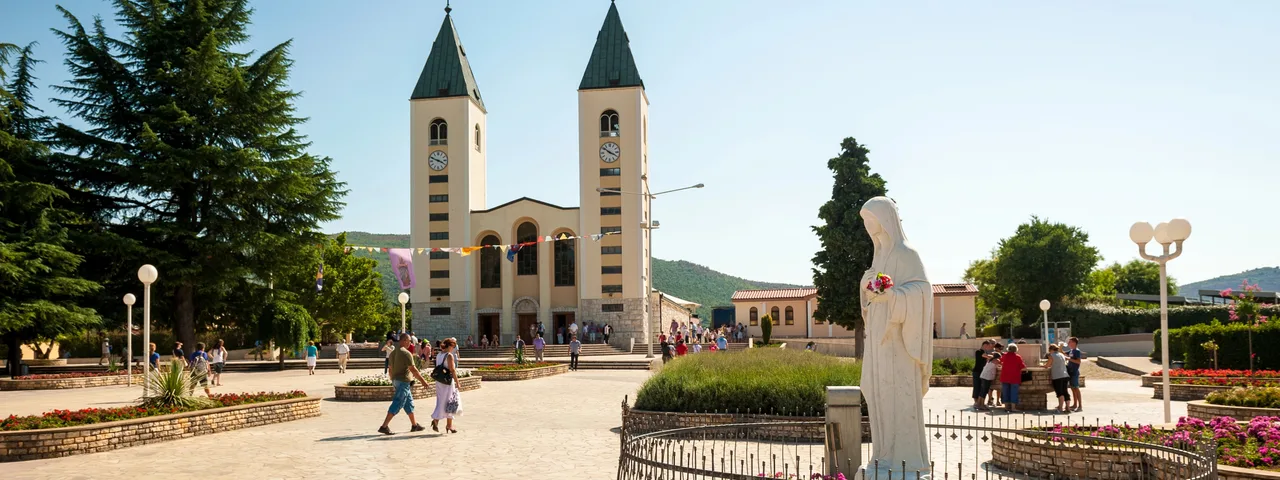 St. James Church in Medjugorje with the Virgin Mary statue in the foreground, garden and square