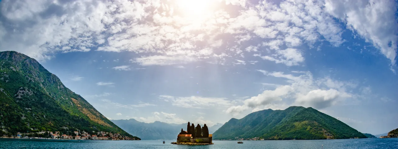 Small passenger boat on turquoise Bay of Kotor with Saint George island monastery in background near Perast
