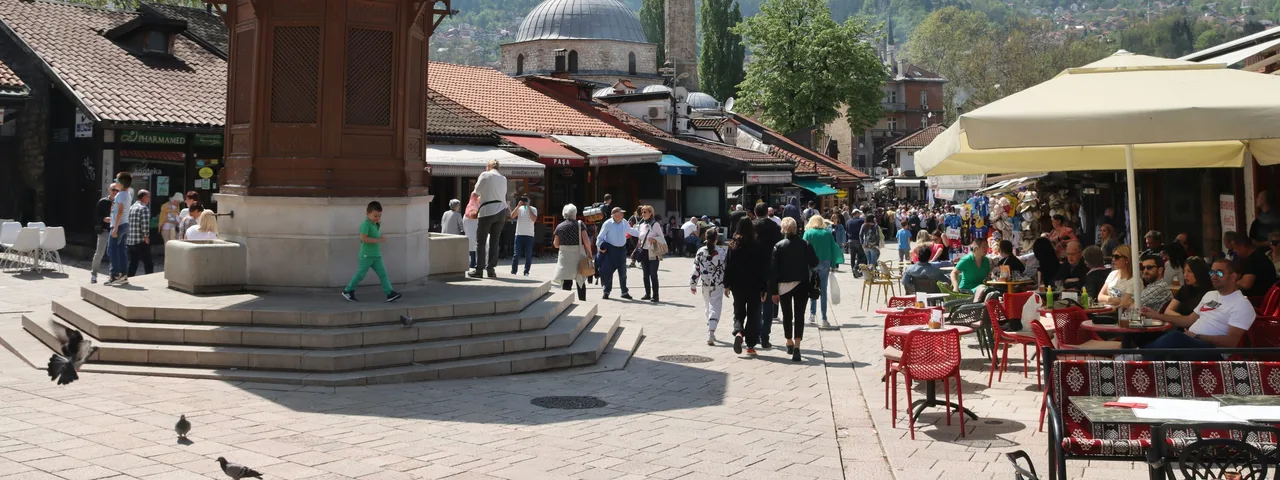 Tourists walking through Baščaršija square in Sarajevo old town with the Ottoman bazaar and Sebilj fountain area visible, Bosnia