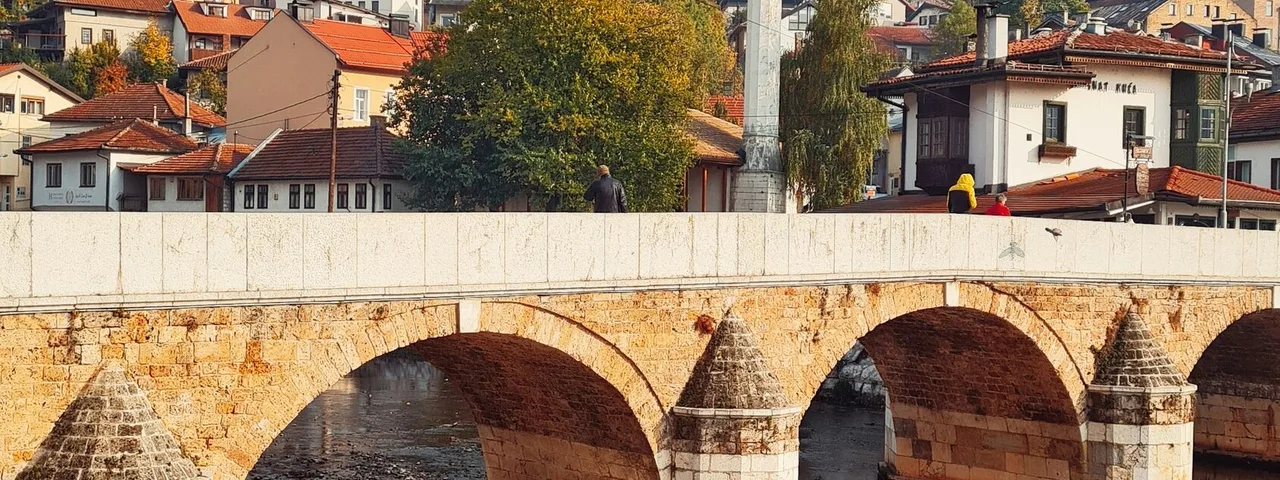 Bridge over the Miljacka River at sunrise with mosque minarets and Sarajevo old town buildings reflected in the calm water, Bosnia
