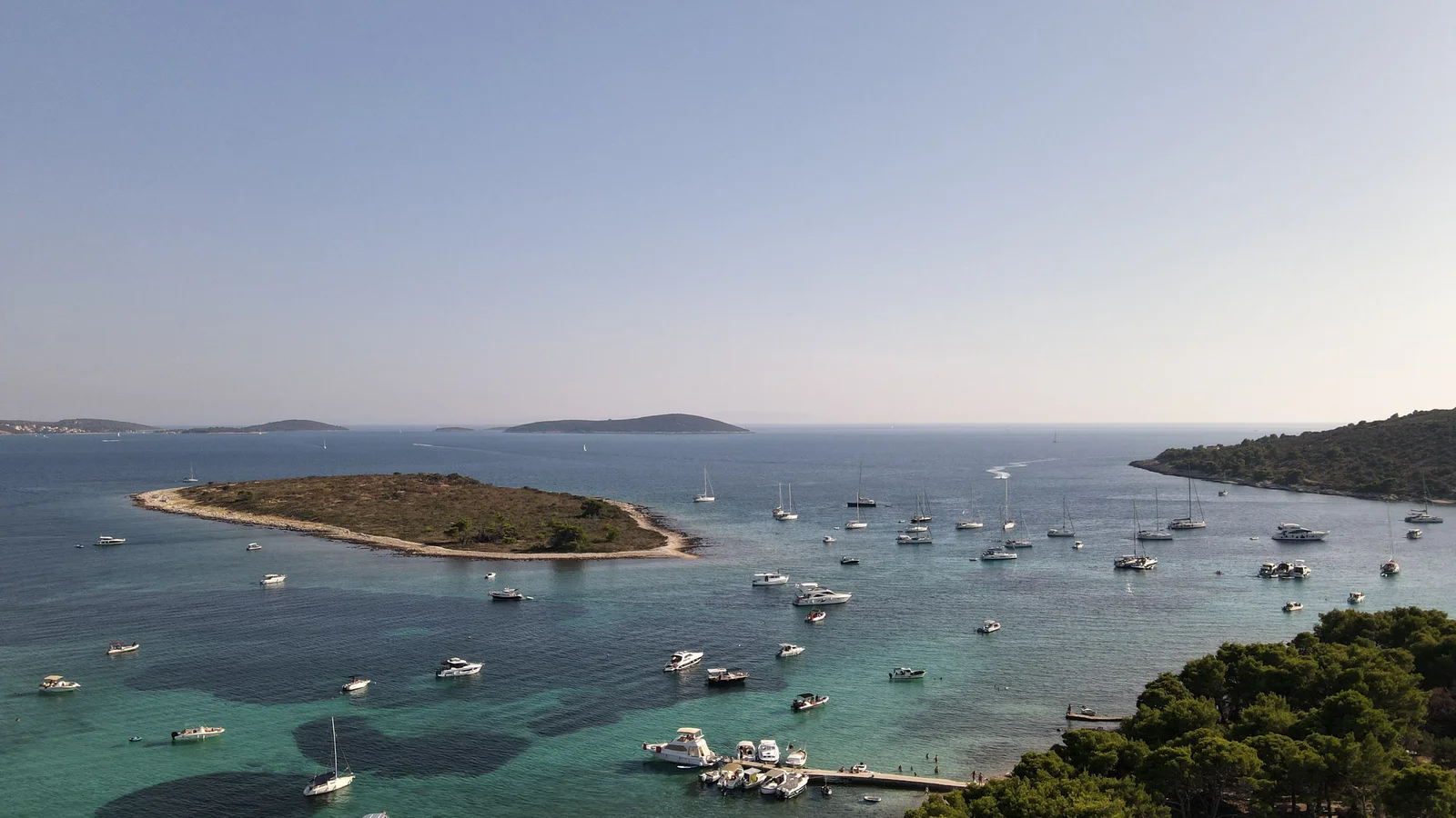 Aerial view of Dalmatian Blue Lagoon near Split with crystal-clear waters, a small island, and numerous boats.
