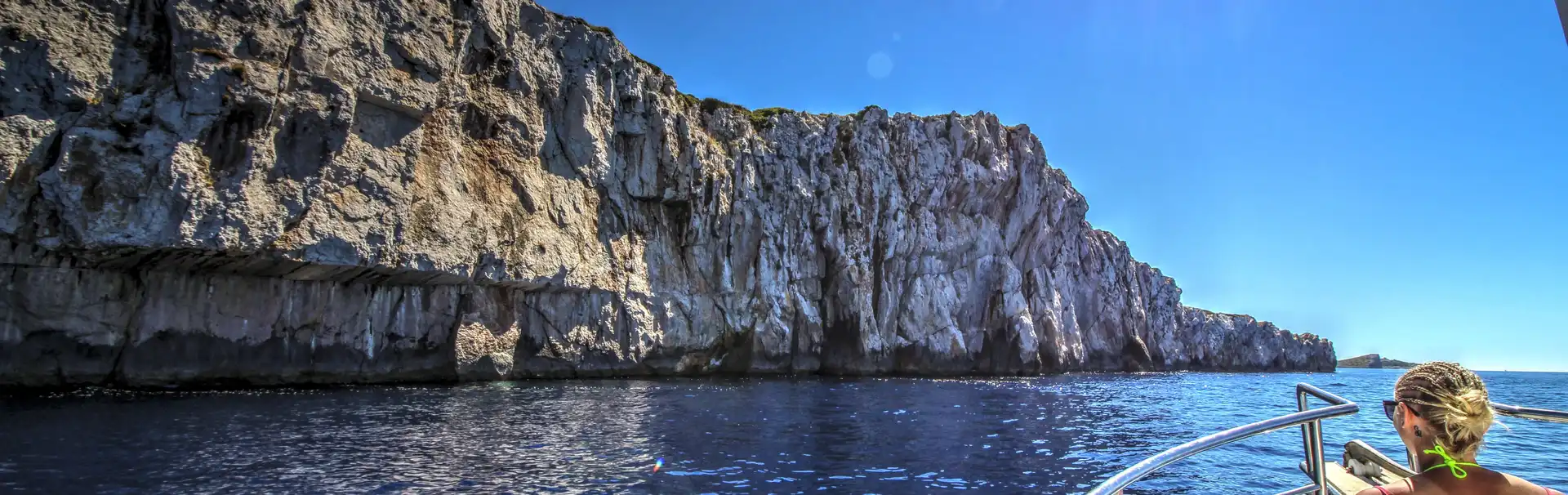 Woman relaxes on boat cruising past sunny Croatian cliffs near Dubrovnik.