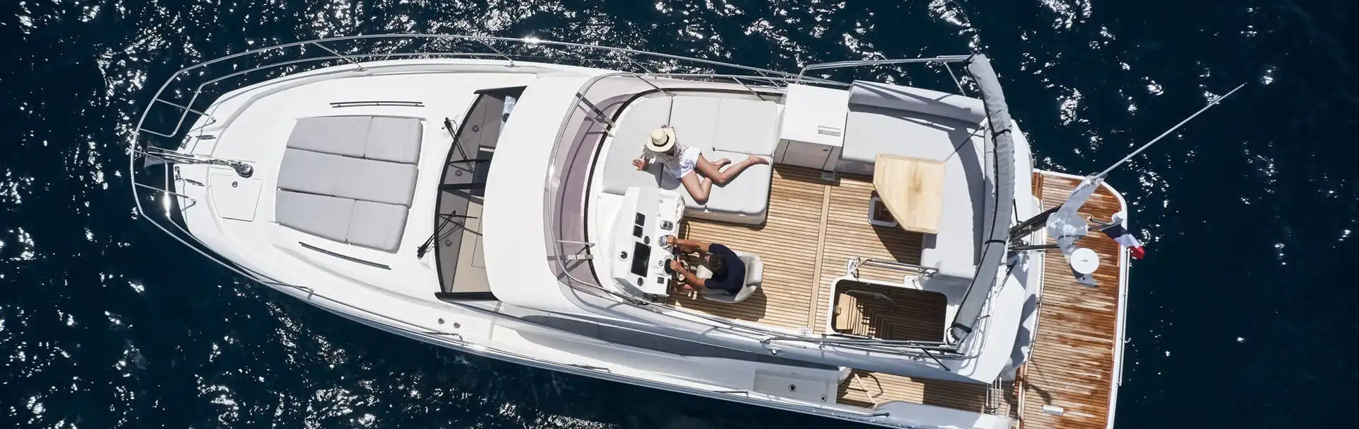 Aerial view of a luxury yacht from our fleet sailing in crystal-clear blue waters, featuring multiple decks, spacious lounging areas, and a sleek white exterior.