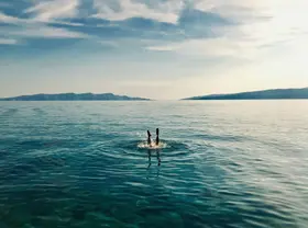 Person diving into the clear turquoise Adriatic Sea with distant islands, showcasing a refreshing private boat tour experience in Croatia.