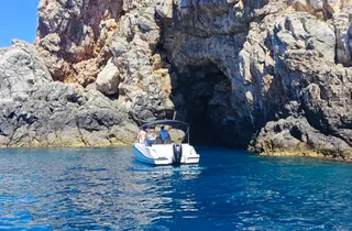 Luxury speedboat approaching a natural cave entrance on the clear blue Adriatic Sea near Dubrovnik, Croatia.