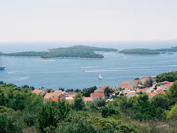 Panoramic view of Hvar, Croatia's stunning Adriatic Sea, with luxury yachts, green islands, and a charming red-roofed coastal village.
