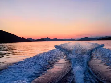 Sunset view from a boat, showing wake trails on calm water surrounded by silhouetted Elaphite islands.