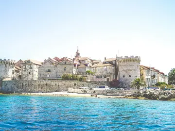 Ancient walled coastal town with stone buildings overlooking crystal-clear turquoise waters of the Adriatic Sea.
