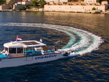 Catamaran cruising clear blue water with historic Dubrovnik cityscape and ancient walls in the background.