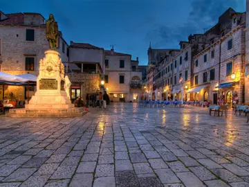 People dining and strolling on the historic Stradun main street of Dubrovnik Old Town at night with glowing lanterns, Croatia
