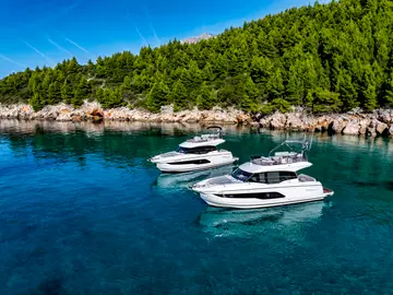 Two luxury motor yachts anchored in crystal-clear blue waters off the lush green coast of Dubrovnik, Croatia.