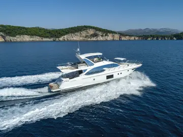Azimut 66 Fly luxury yacht cruising on deep blue Adriatic waters, leaving a white wake against a green, hilly coastline.