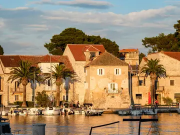 Picturesque Milna village on Brač Island, Croatia, with historic stone buildings, palm trees, and boats docked in its serene harbor at sunset.