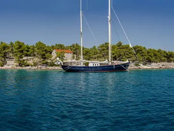 A luxury private sailboat anchored in crystal-clear blue waters next to a lush green Dalmatian island, perfect for serene escapes.