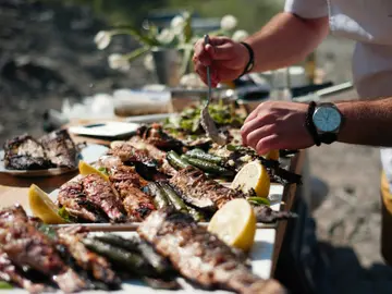 Close-up of a man serving freshly grilled fish and vegetables with lemon at an outdoor Mediterranean dining experience.