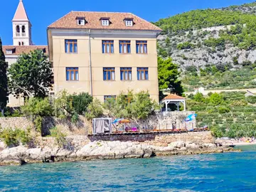 Historic Franciscan Monastery and bell tower on Hvar island's rocky coast, viewed from the turquoise Adriatic Sea.