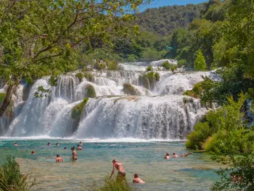 Tourists swimming in crystal-clear turquoise pool beneath Skradinski Buk waterfall at Krka National Park, Dalmatia, Croatia