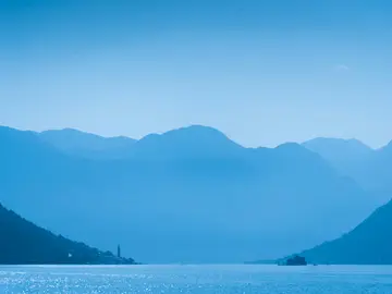 Layered misty blue mountains over the Bay of Kotor with the bell tower of Perast visible on the shoreline, Montenegro