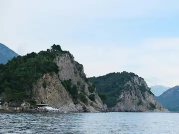 Pine-covered limestone cliffs rising from the turquoise Adriatic at Petrovac, on the southern Montenegrin coast