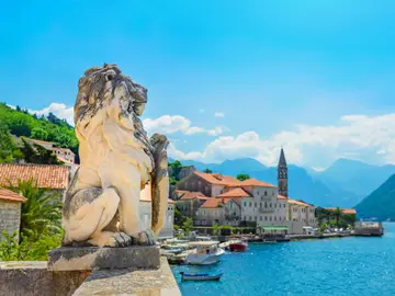 Stone lion statue on waterfront terrace with village of Perast and Bay of Kotor in background, Montenegro