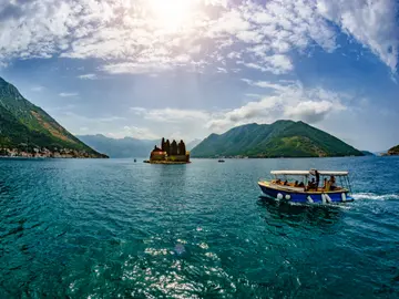 Small passenger boat on turquoise Bay of Kotor with Saint George island monastery in background near Perast