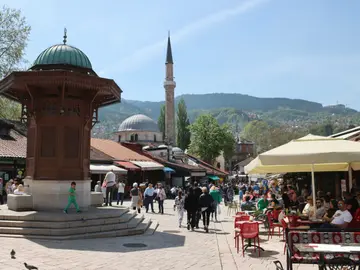 Tourists walking through Baščaršija square in Sarajevo old town with the Ottoman bazaar and Sebilj fountain area visible, Bosnia