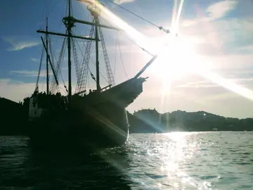 Historic sailing ship silhouetted against sunset in Dubrovnik harbor, offering unique adventure cruises along Croatian coast