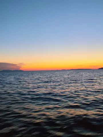 Serene sunset over calm sea with distant islands silhouetted against colorful sky gradient