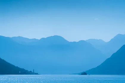 Layered misty blue mountains over the Bay of Kotor with the bell tower of Perast visible on the shoreline, Montenegro