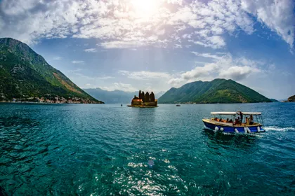 Small passenger boat on turquoise Bay of Kotor with Saint George island monastery in background near Perast