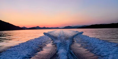 Sunset view from a boat, showing wake trails on calm water surrounded by silhouetted Elaphite islands.