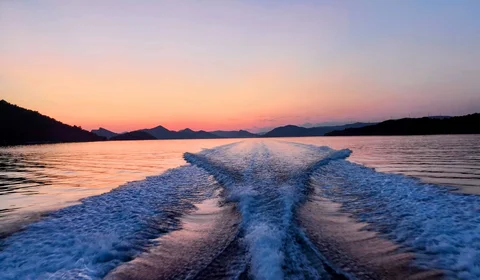 Sunset view from a boat, showing wake trails on calm water surrounded by silhouetted Elaphite islands.