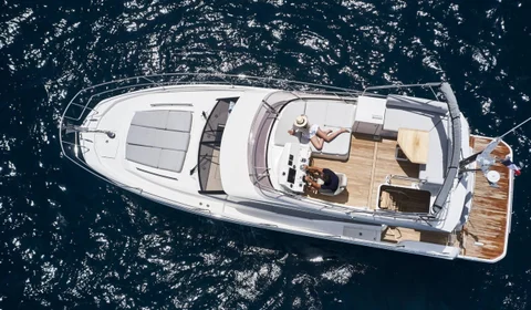 Aerial view of a luxury yacht from our fleet sailing in crystal-clear blue waters, featuring multiple decks, spacious lounging areas, and a sleek white exterior.