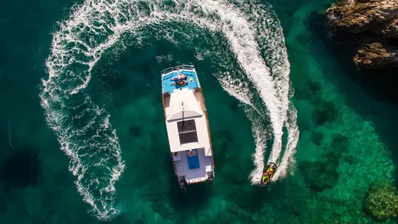 Aerial view of a catamaran and jet ski making waves in clear turquoise adriatic sea near Dubrovnik. Summer vacation scene.