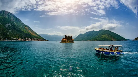 Small passenger boat on turquoise Bay of Kotor with Saint George island monastery in background near Perast