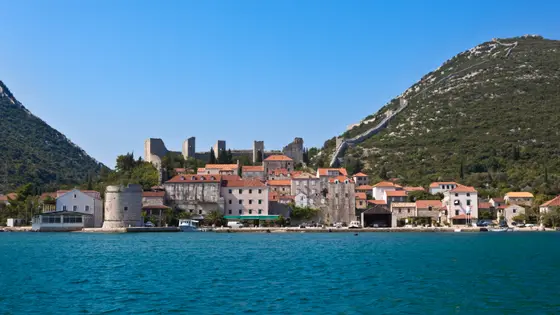 Ston town waterfront with stone buildings, round medieval defensive tower and ancient walls climbing the green hillside, Dalmatia, Croatia