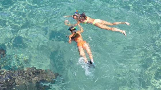 Two people snorkeling in crystal-clear turquoise waters near Blue Cave on a sunny day.