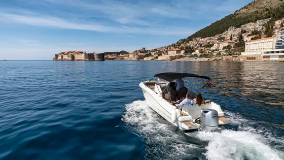 Luxury boat cruising blue Adriatic Sea with Dubrovnik Old Town city walls and scenic coastline in Croatia.