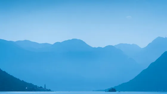 Layered misty blue mountains over the Bay of Kotor with the bell tower of Perast visible on the shoreline, Montenegro